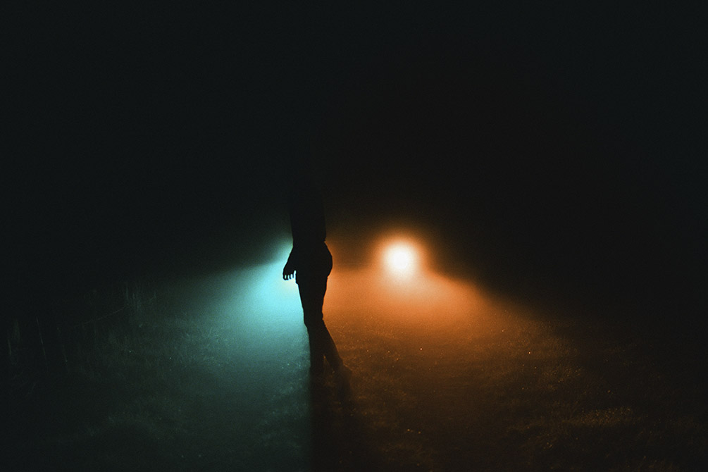 фары автомобиля освещают человека в темноте
